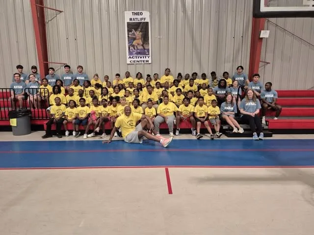 A large summer program group gathered on the center gym bleachers